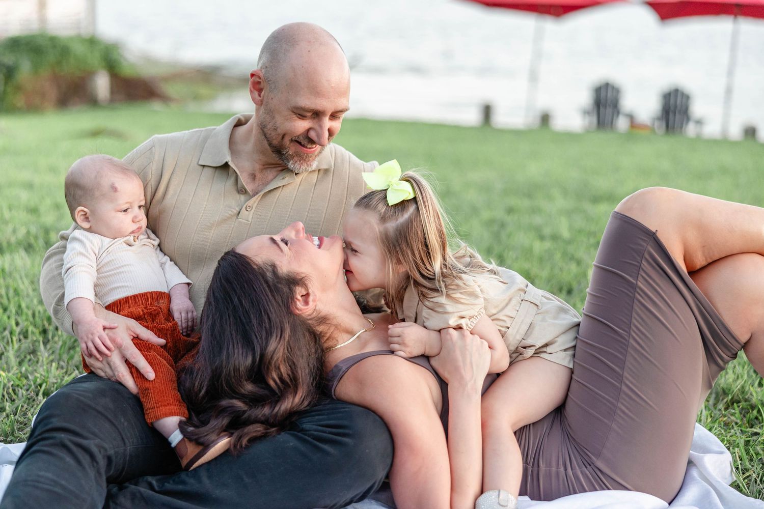 Happy family relaxing on grass, mother lying down with daughter kissing her cheek and baby.