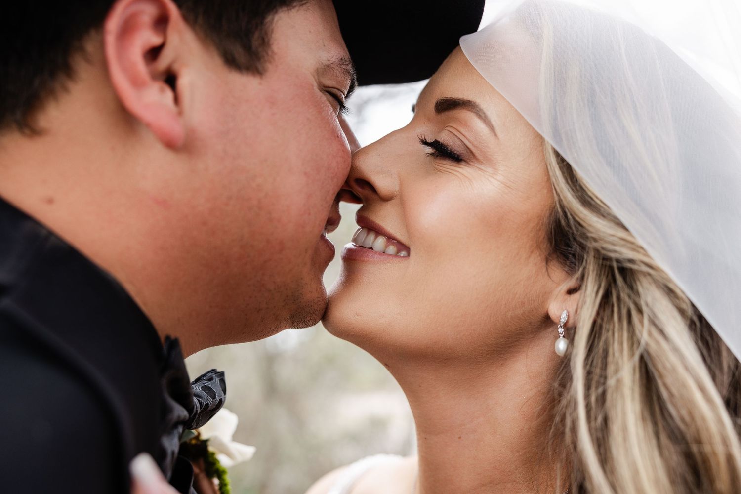 Close-up of smiling bride and groom about to kiss, bride wearing veil and drop earrings.