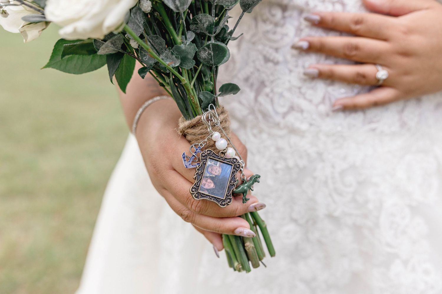 Bride holds white floral bouquet with a memorial photo charm tied with twine on her wedding day.