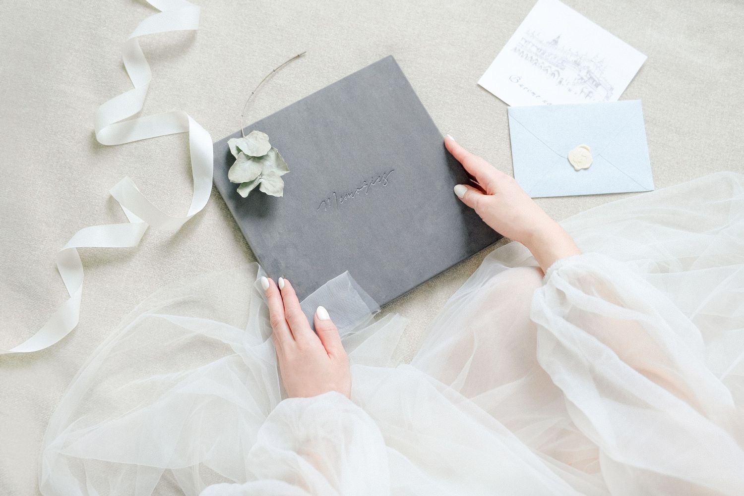 Hands in white tulle dress holding gray velvet wedding photo album with floral decoration.