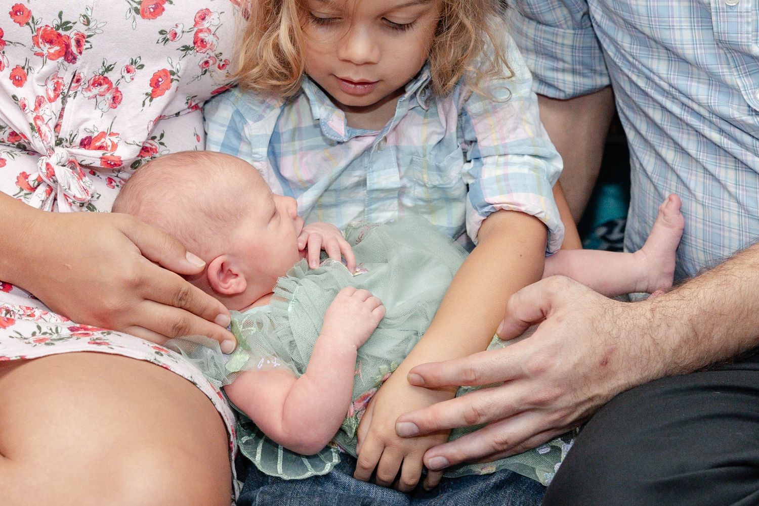 Young child holding newborn baby sibling while parents support them on their laps.