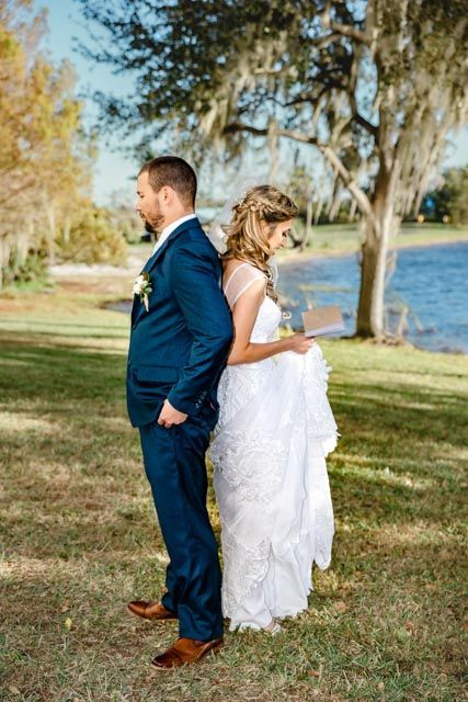 Bride and groom stand back-to-back reading vows by a lakeside under Spanish moss-draped oak trees.