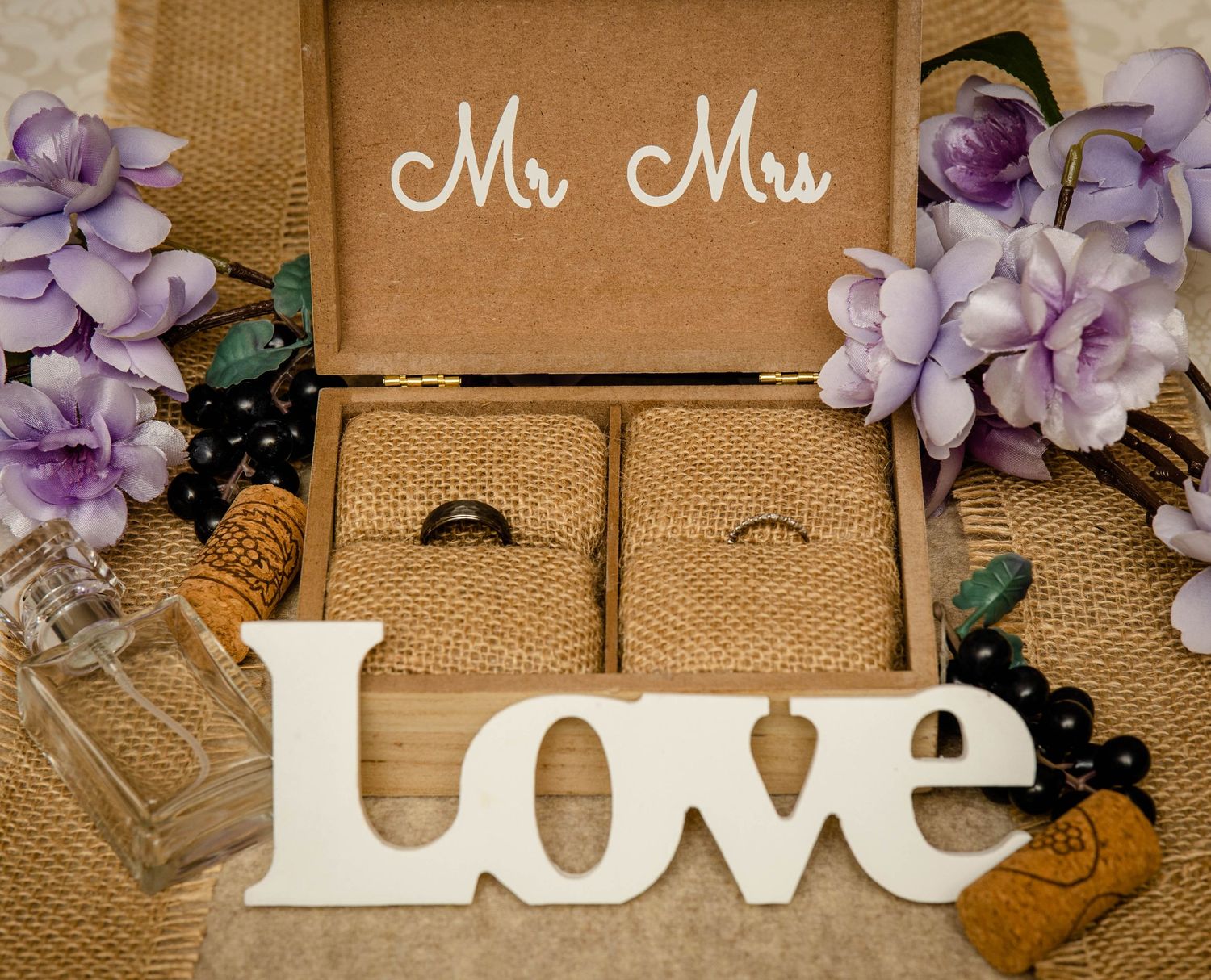 Rustic Mr and Mrs ring box with Love sign, purple flowers, and wedding rings.