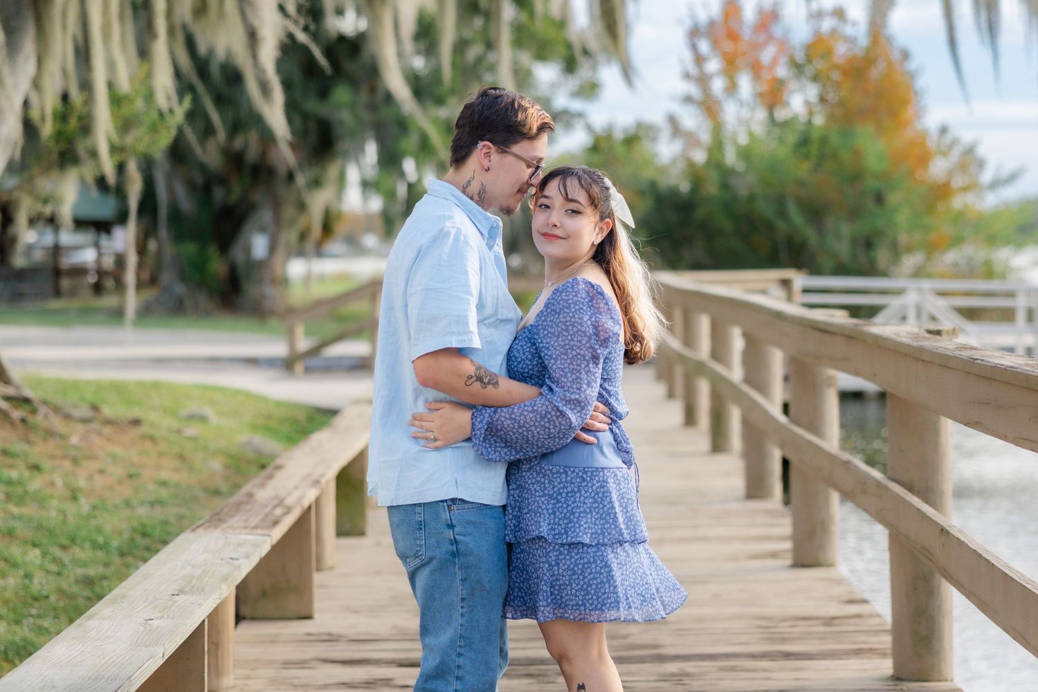 A couple shares a tender embrace on a wooden bridge surrounded by lush trees and soft light.