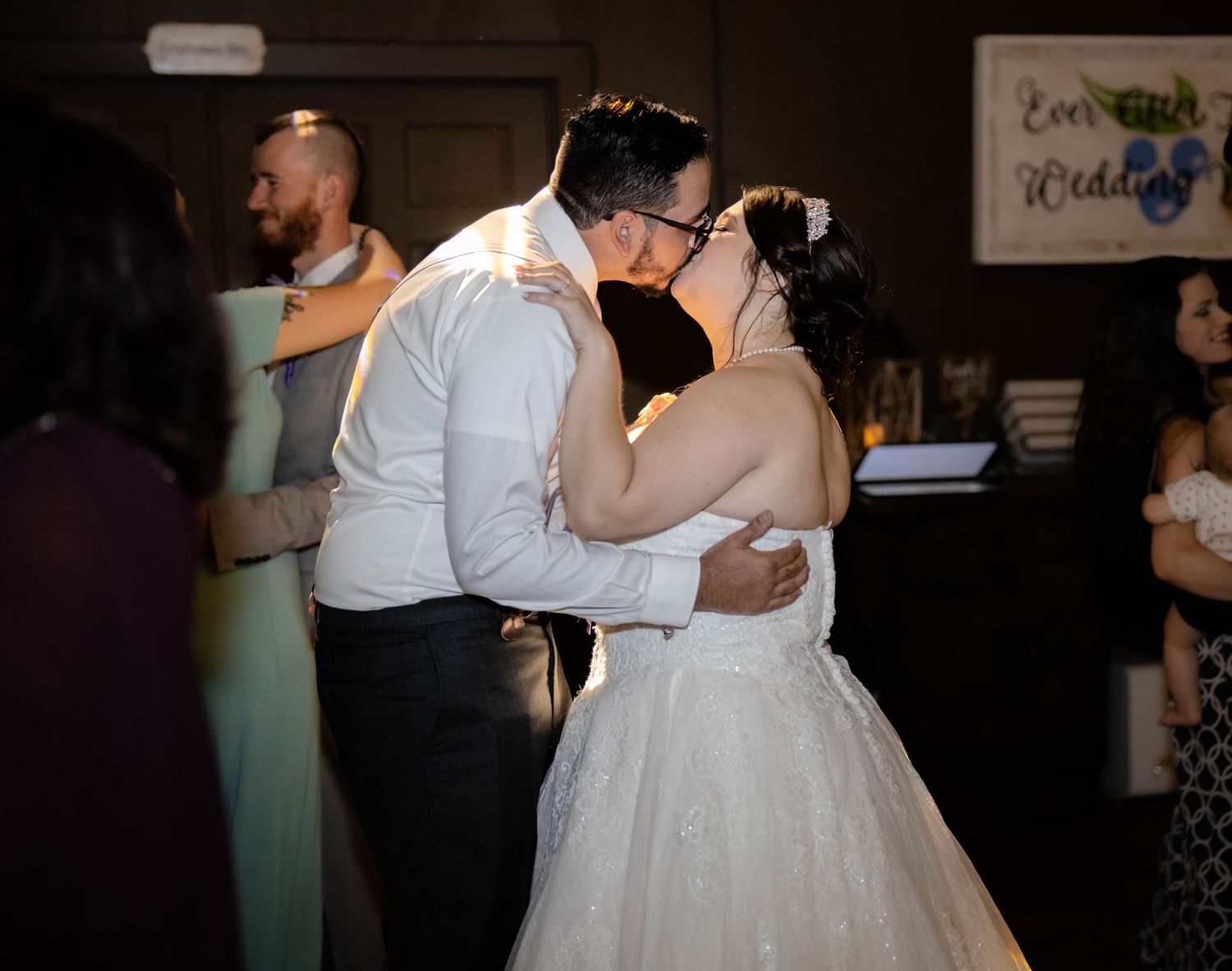 Newlywed couple sharing a first kiss on the dance floor surrounded by wedding guests.