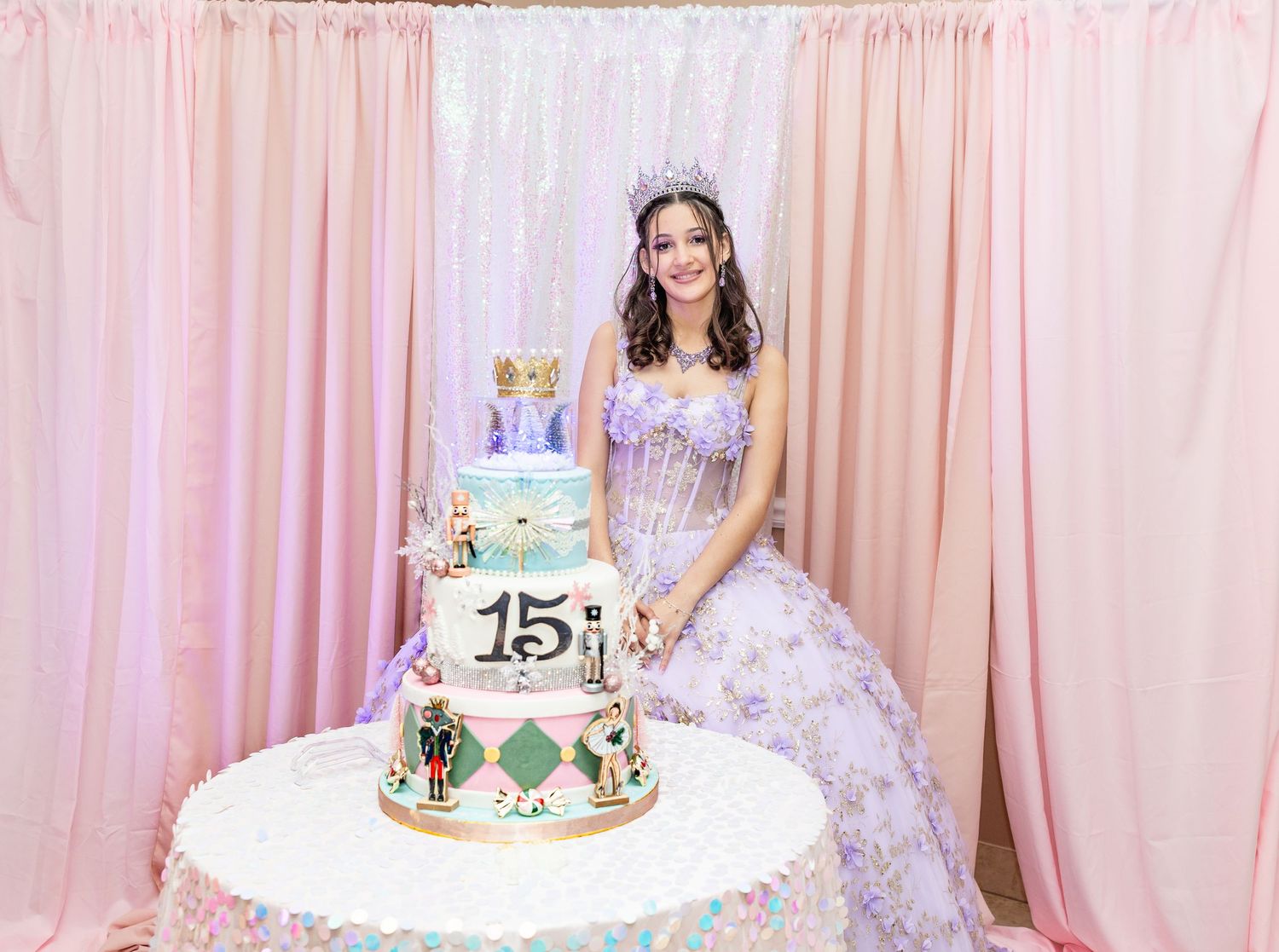 Quinceañera girl in lavender ball gown and tiara poses beside her decorated 15th birthday celebration cake.