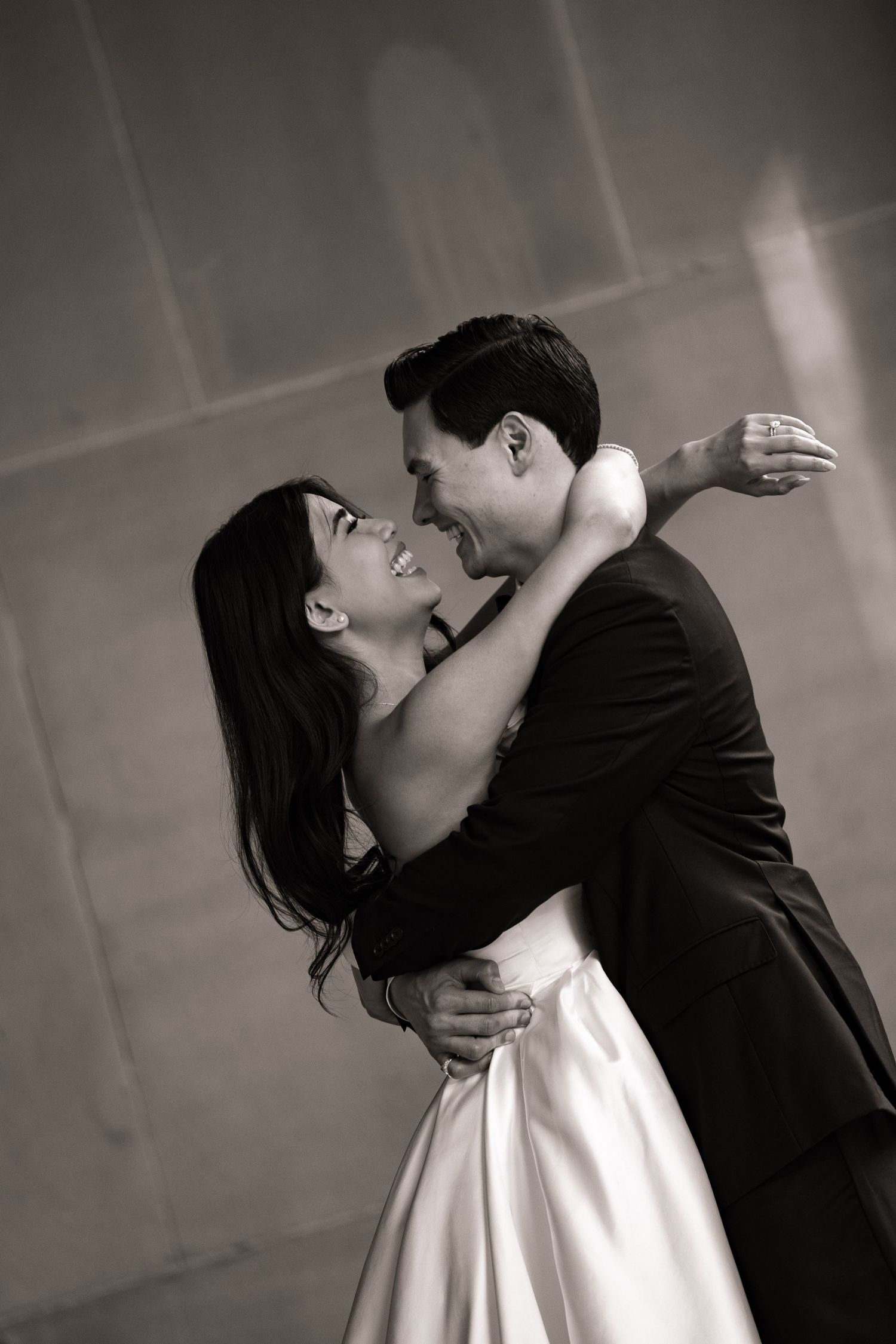 Black and white photo of a bride and groom sharing a joyful embrace, smiling at each other during their first dance.