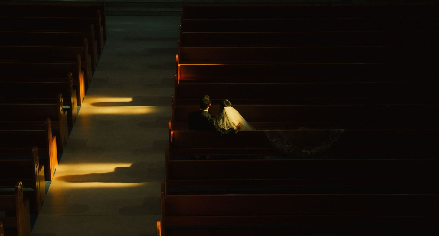 Couple sitting in a dimly lit church pew with warm golden light streaming through windows.