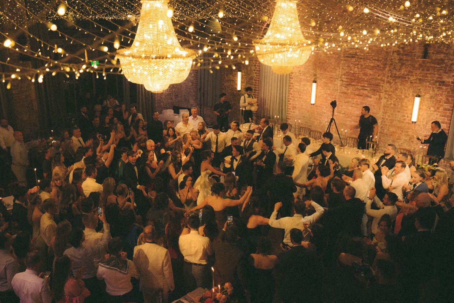 Elegant wedding reception with crystal chandeliers, string lights, and guests dancing on a crowded dance floor.