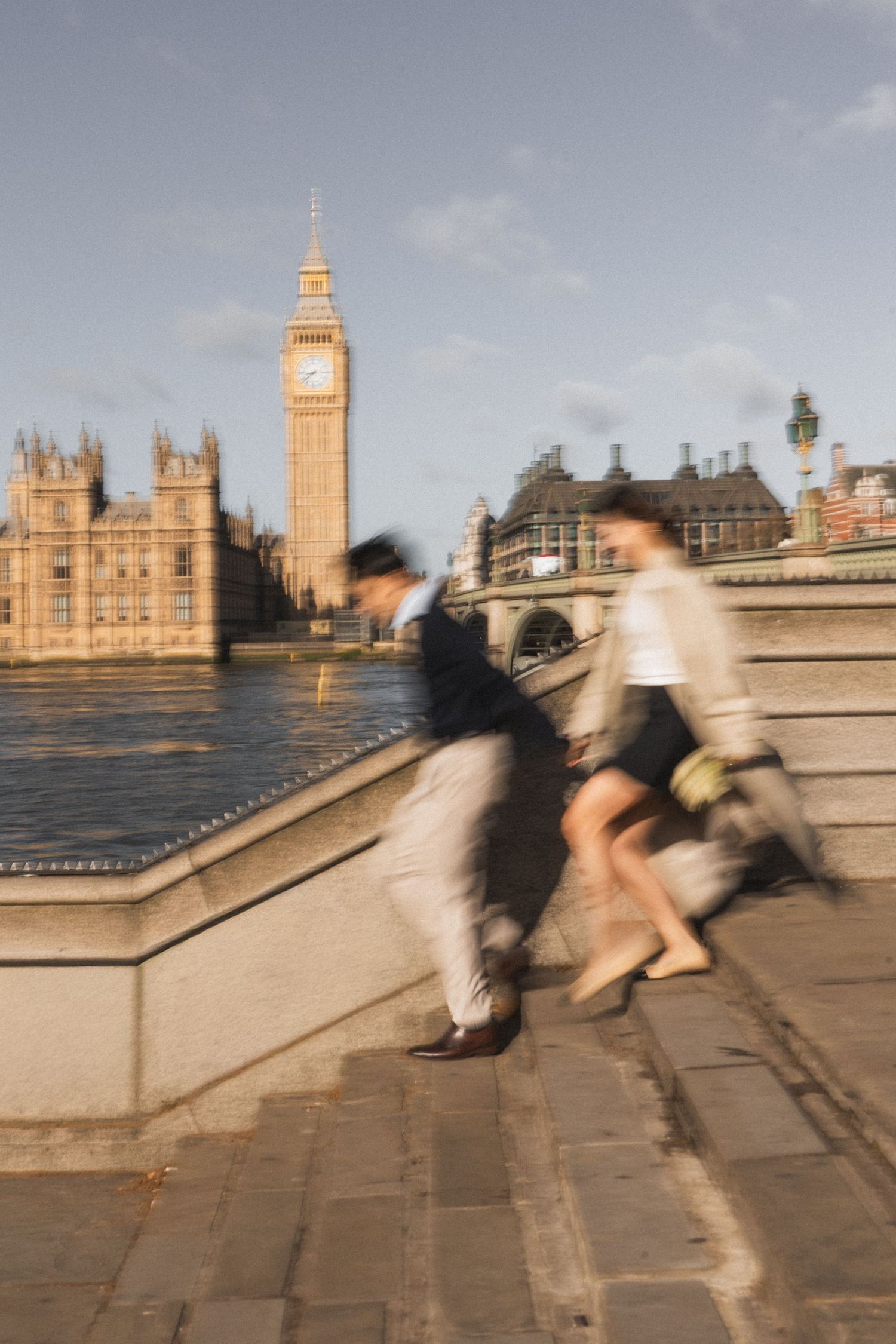 Motion blur photo of couple climbing steps near Big Ben and River Thames in London.