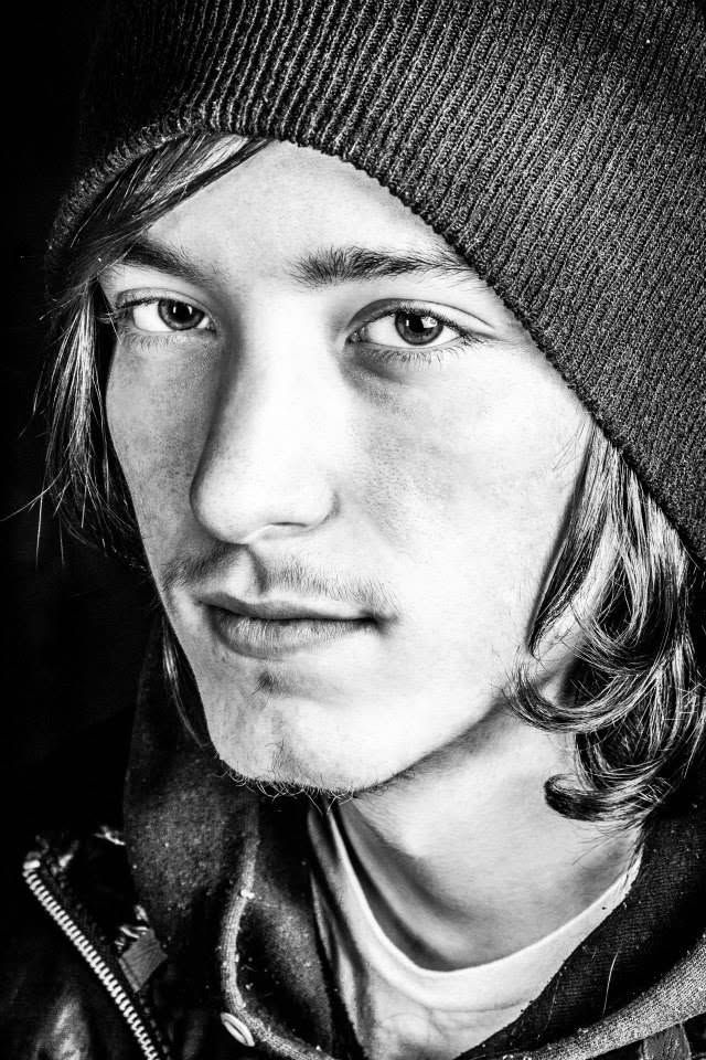 Black and white close-up portrait of a young man in a beanie hat with medium-length hair.
