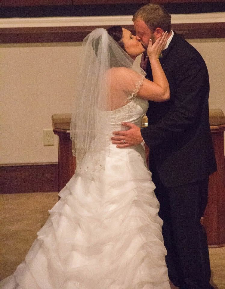 Bride and groom share their first kiss at the altar, bride wearing a white ruffled gown and veil.