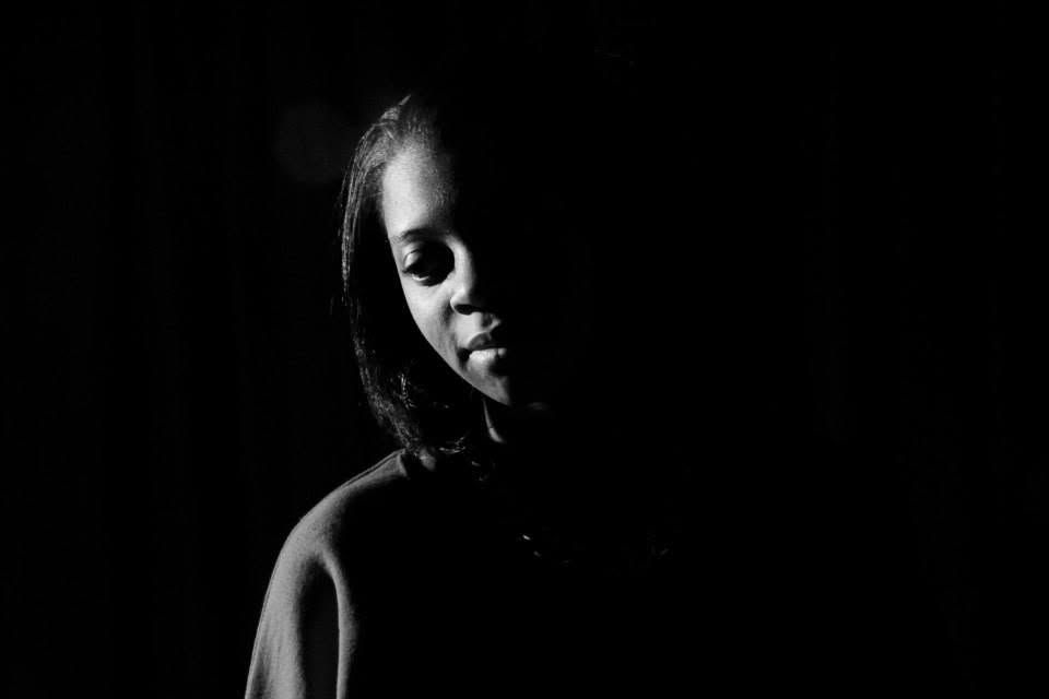 Black and white portrait of a young woman with soft lighting against a dark background.