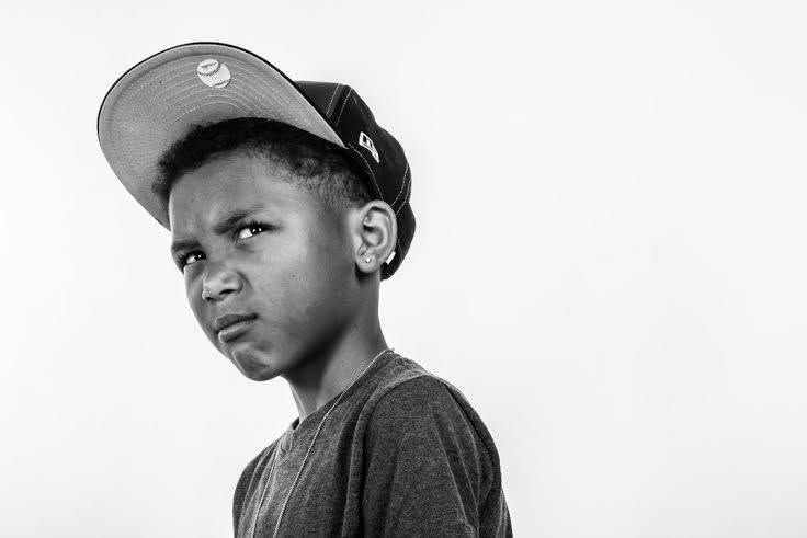 Black and white portrait of a young boy in a snapback cap with a serious expression.