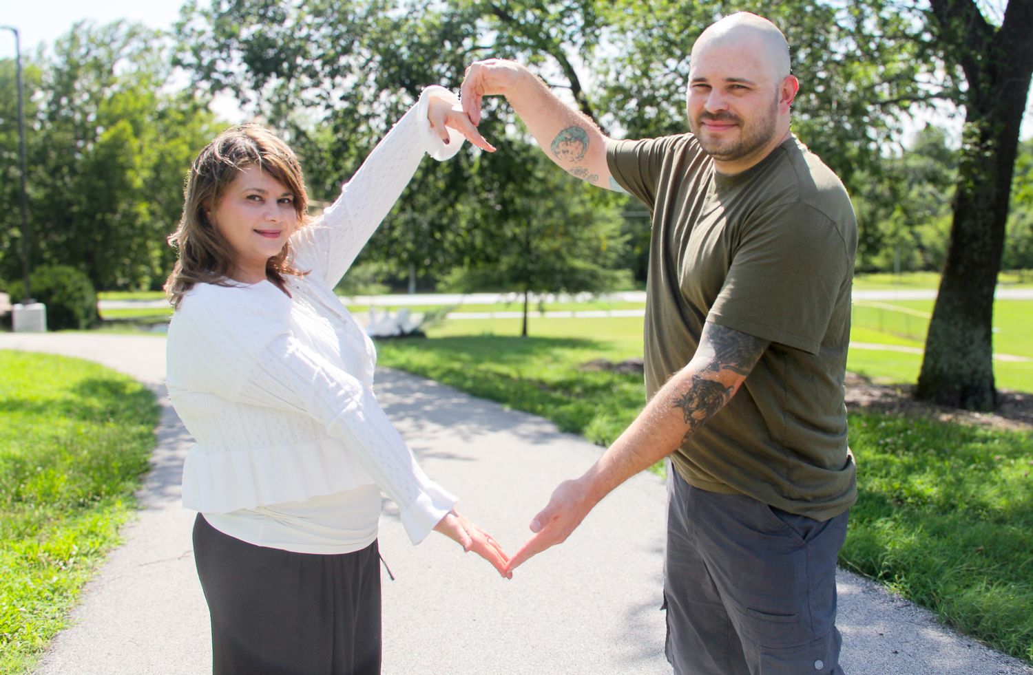 Couple dancing outdoors on a park path, holding hands with arms raised in a sunny green setting.