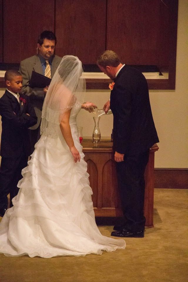 Bride and groom performing a sand ceremony at their wedding altar, officiant and young boy standing nearby.