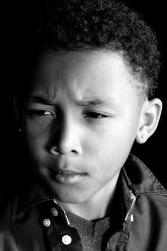Dramatic black and white portrait of a young boy with a thoughtful, serious expression wearing a jacket.