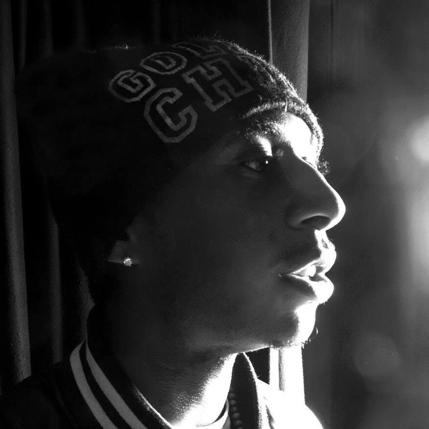 Black and white profile portrait of young man in beanie hat and varsity jacket looking toward window light.