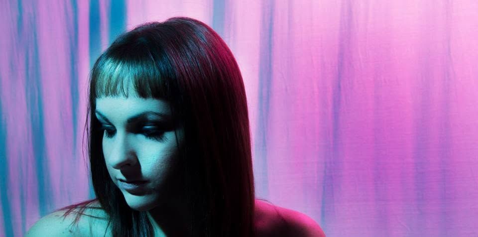 Woman with dark hair posing in moody neon pink and blue lighting against a colorful abstract background.