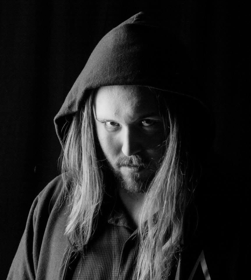 Man with long hair wearing dark hood, moody black and white dramatic portrait photography.