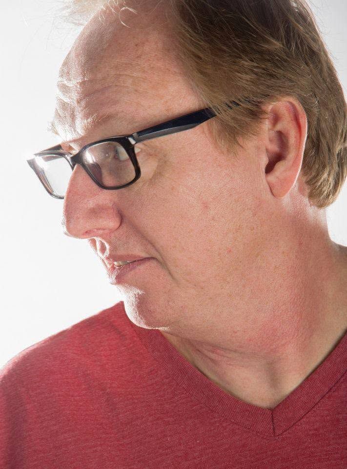 Middle-aged man wearing black rectangular glasses in profile view against a white background.