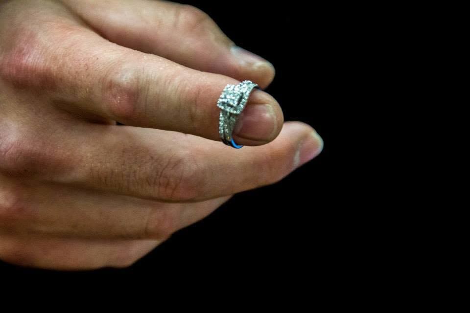 Close-up of a hand wearing a sparkling diamond engagement ring with intricate band detail on black background.