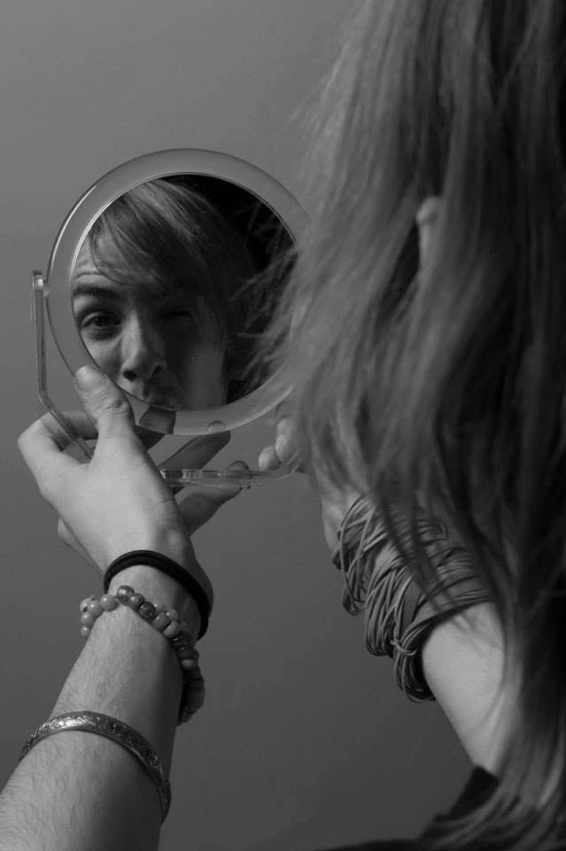 Woman examining her reflection in a small round mirror, wearing bracelets, black and white photo.