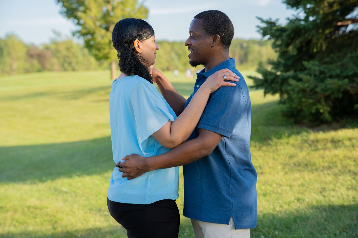 A couple embracing outdoors on a green lawn, wearing matching blue shirts, sharing a tender moment.