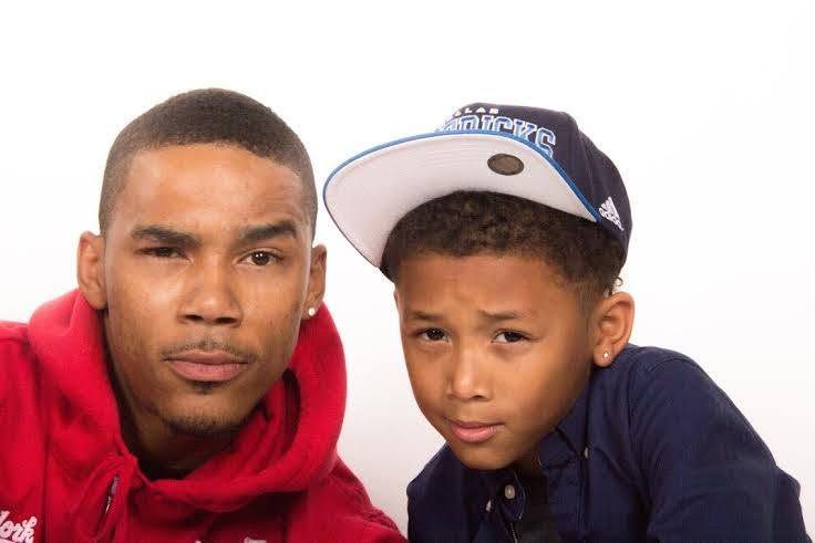 A young boy wearing a snapback cap poses with an older teen in a red hoodie against a white background.