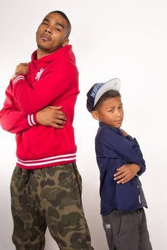 Two males in matching poses with arms crossed, one in red hoodie and camo pants, other in blue jacket and flat cap.