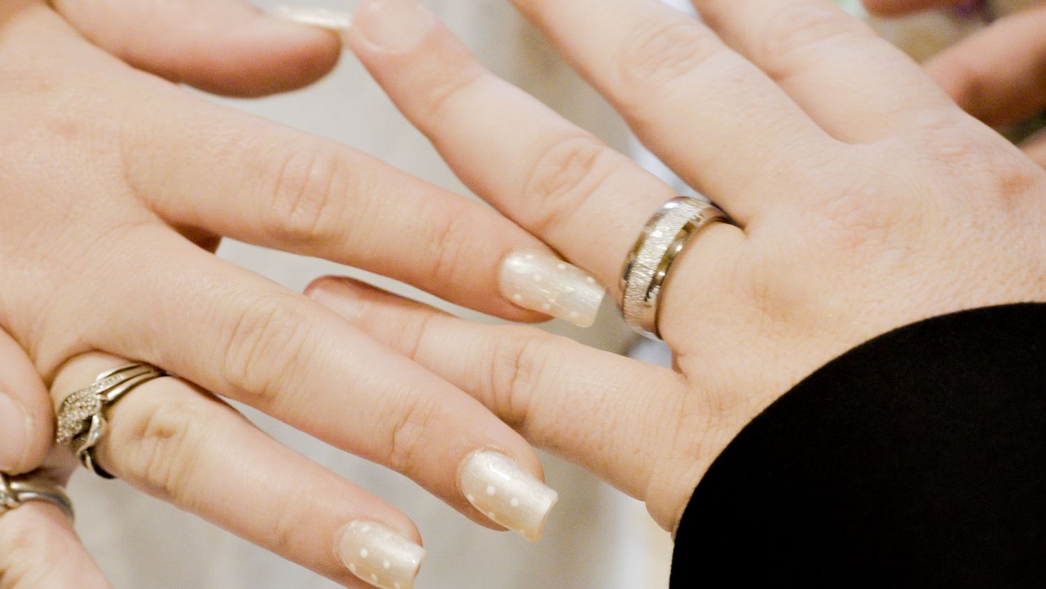 Close-up of two hands displaying wedding rings, with gold nail polish on the bride's manicured nails.