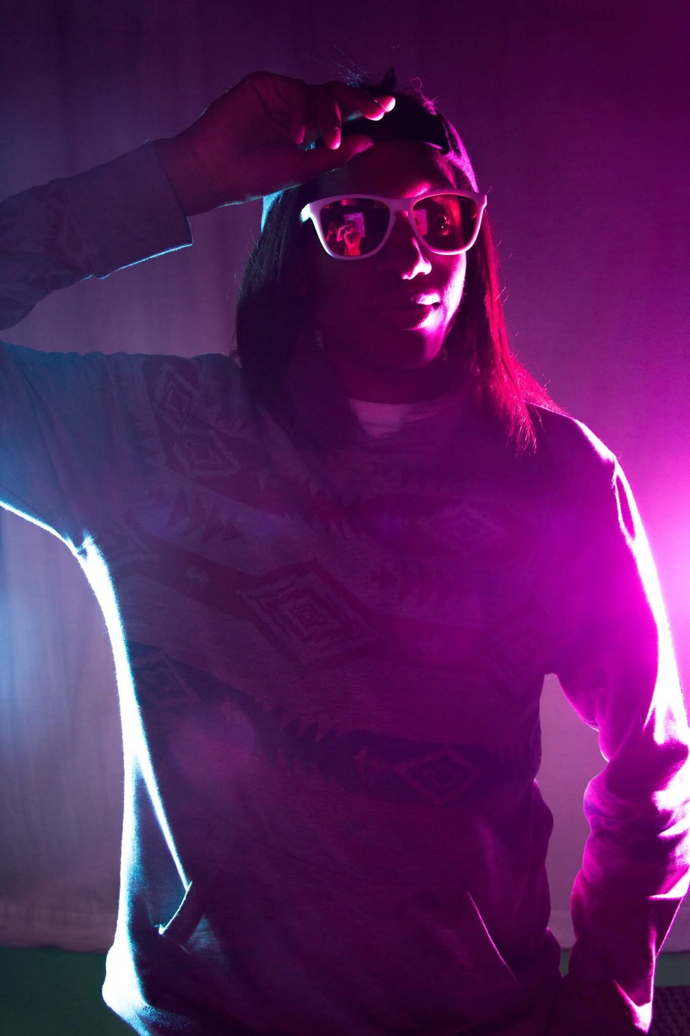 Person wearing sunglasses posing under dramatic purple and pink neon lighting with tattoos.