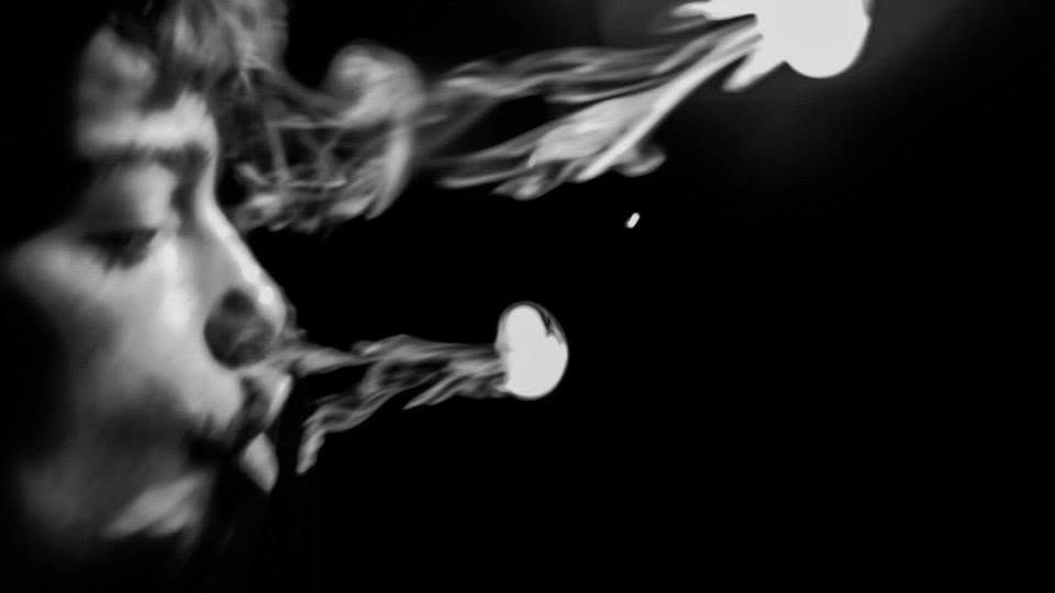 Black and white close-up of a person exhaling smoke in dramatic low-key lighting.