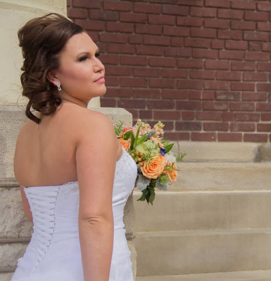 Bride in a white strapless corset gown holds a peach rose bouquet while posing on stone steps.