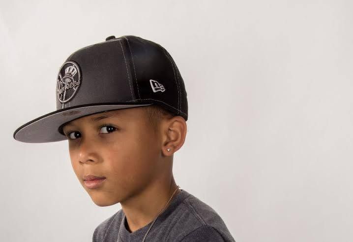 Young boy wearing a black New Era snapback cap with a metallic logo, posing against a white background.