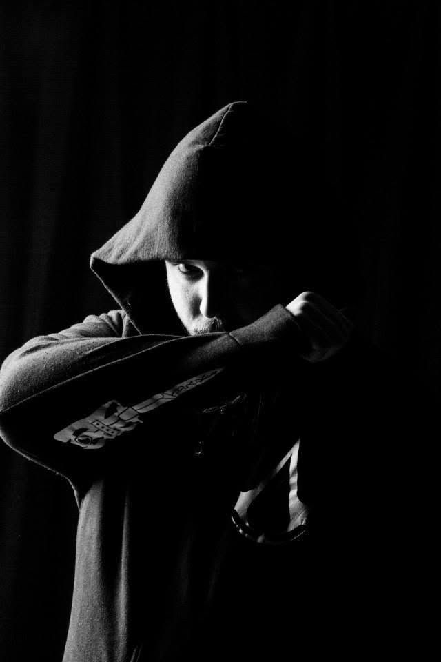 Mysterious figure in a hooded sweatshirt photographed in dramatic black and white low-key lighting.
