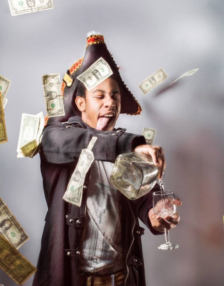 Child in pirate costume with sombrero poses with glass while dollar bills fly around dramatically.