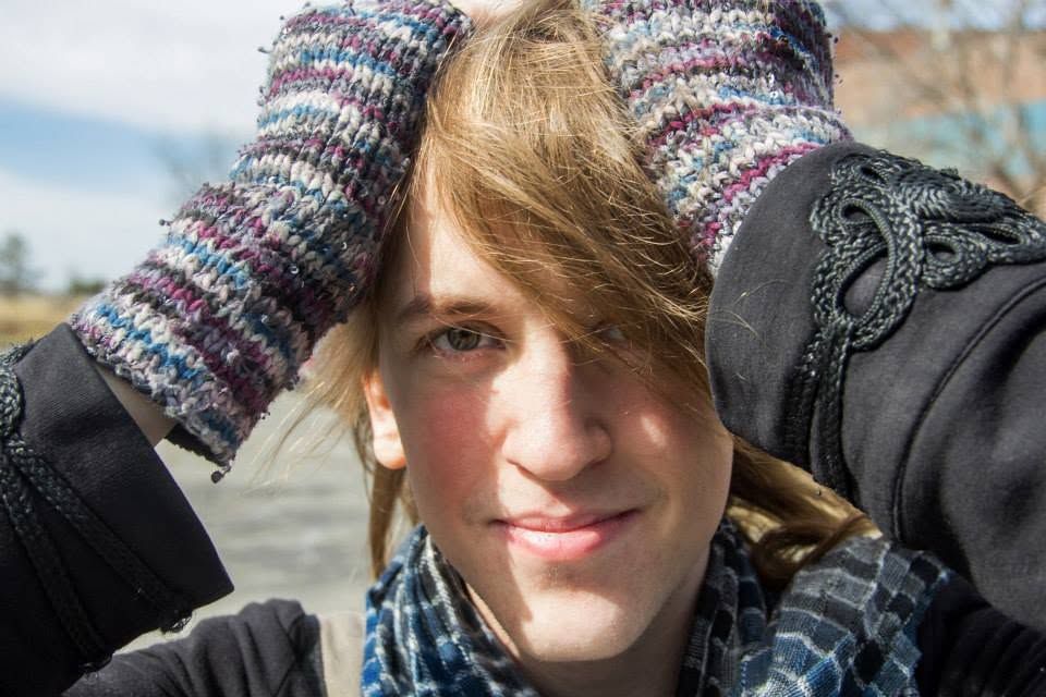 Young woman smiling outdoors wearing knit mittens raised near her head and a colorful scarf.
