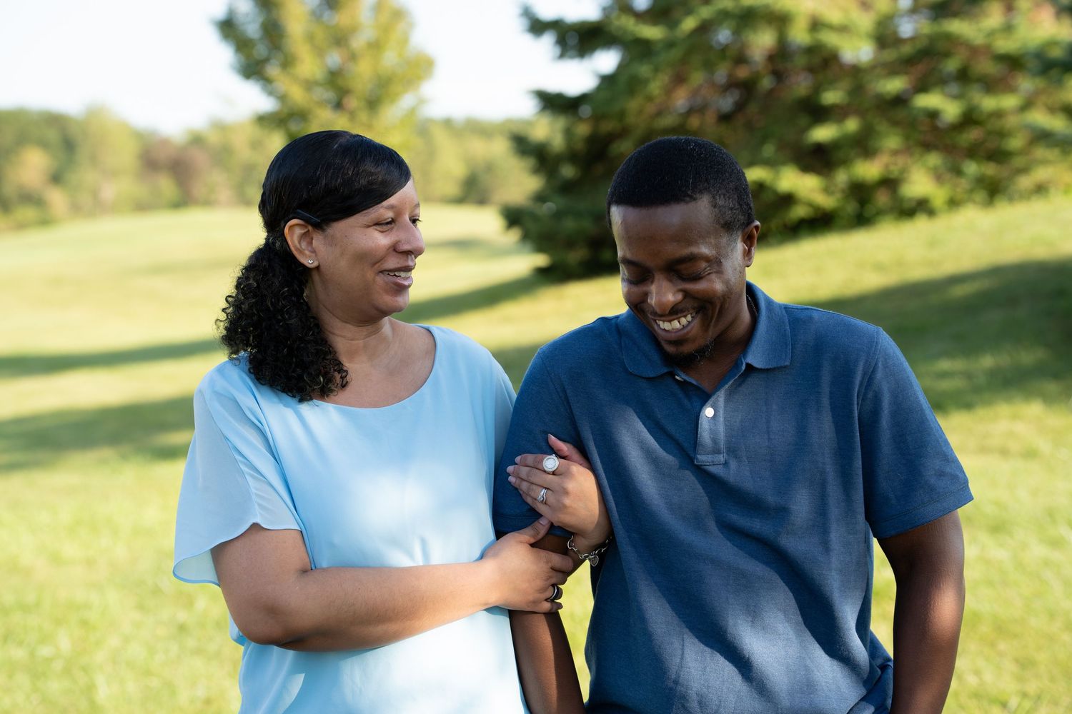 Two people smiling and walking together outdoors in a lush green park on a sunny day.