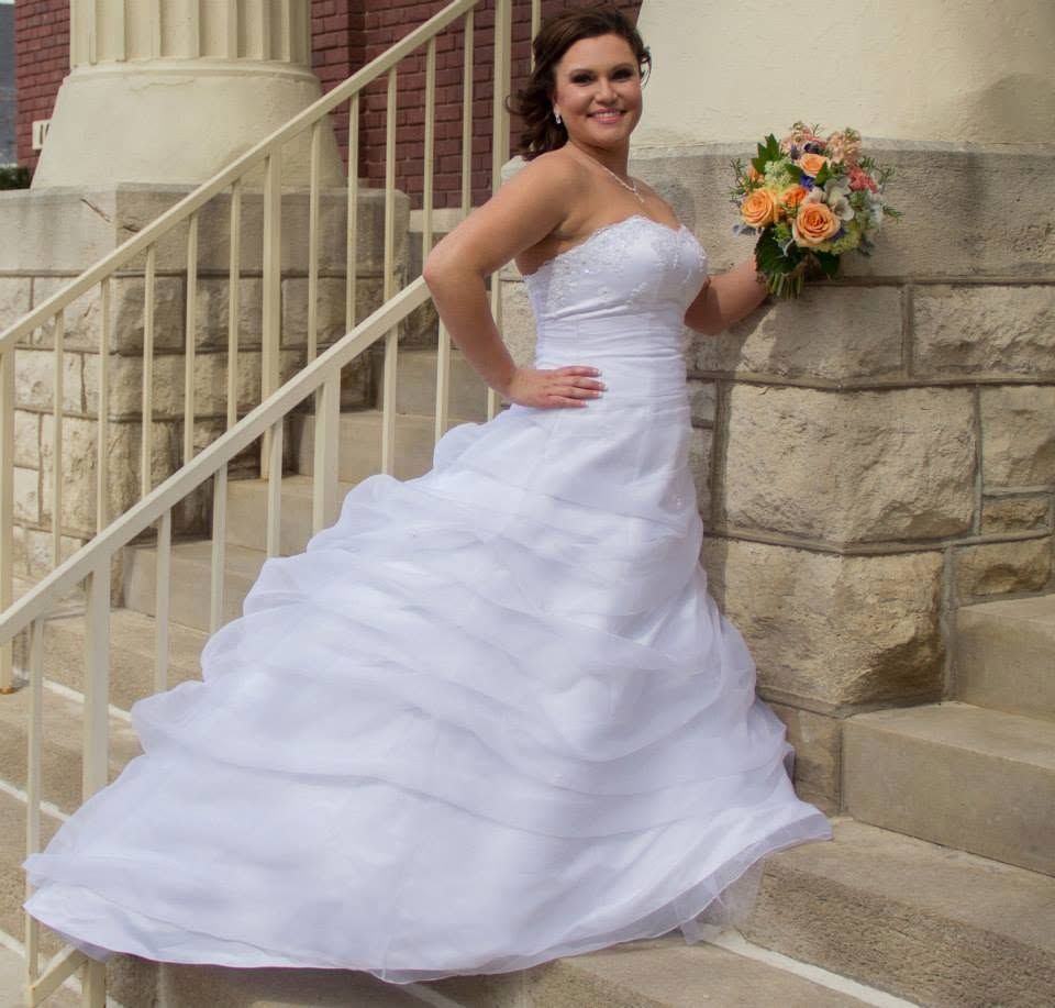 Bride in strapless white ball gown wedding dress holding pink bouquet, posing on stone steps.