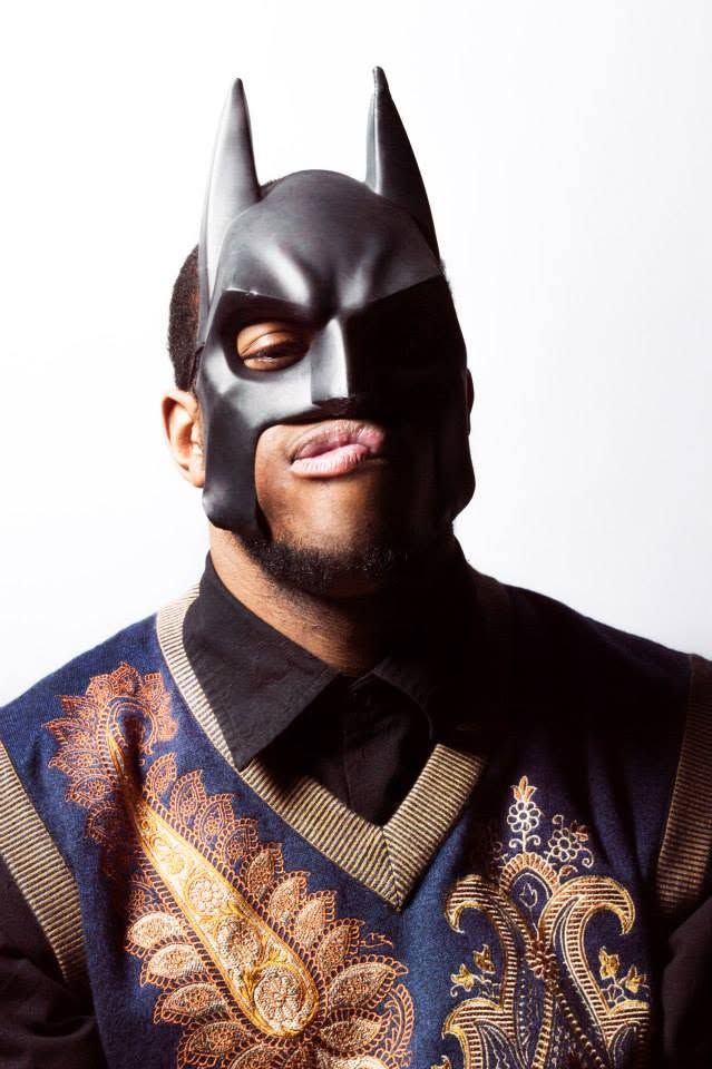 Man wearing Batman mask and ornate blue gold embroidered vest making a funny face against white background.