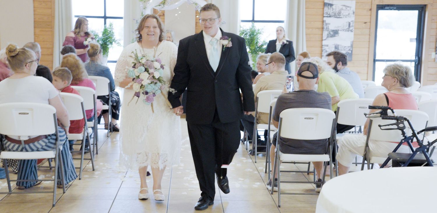 Bride and groom walk down the aisle hand in hand during their wedding ceremony with seated guests.