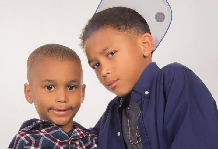 Two young boys posing together for a portrait photo, one wearing a plaid shirt and the other a blue dress shirt.