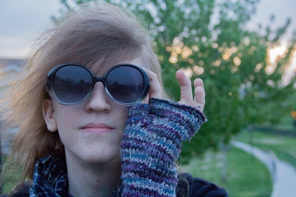 Young woman wearing large round sunglasses and knit fingerless gloves outdoors.