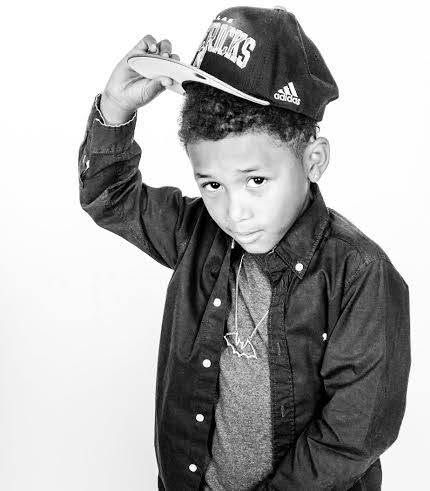A stylish young boy in a denim jacket tips his snapback cap in a black and white studio portrait.