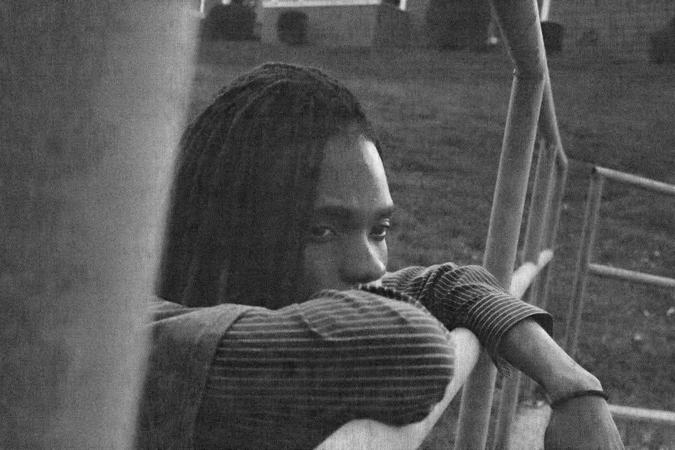 Black and white photo of a person with dreadlocks resting on a railing in a contemplative pose.