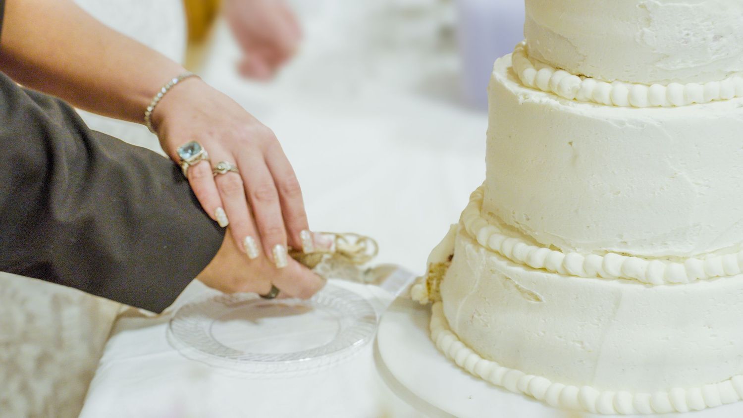 Couple cutting a elegant three-tier white wedding cake with pearl decorations at a reception.