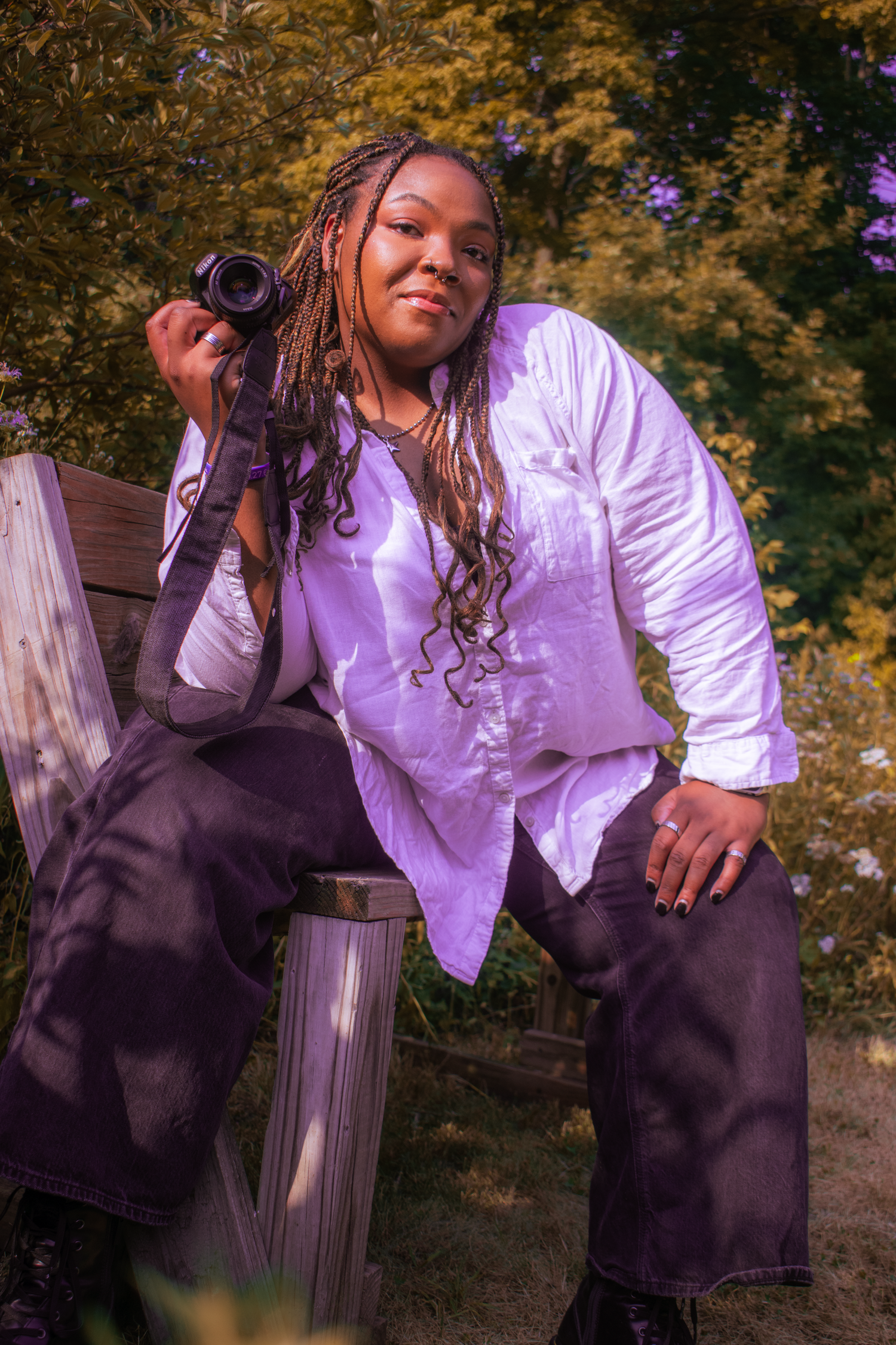 Young woman photographer sitting on bench holding camera wearing white shirt in a Milwaukee park.
