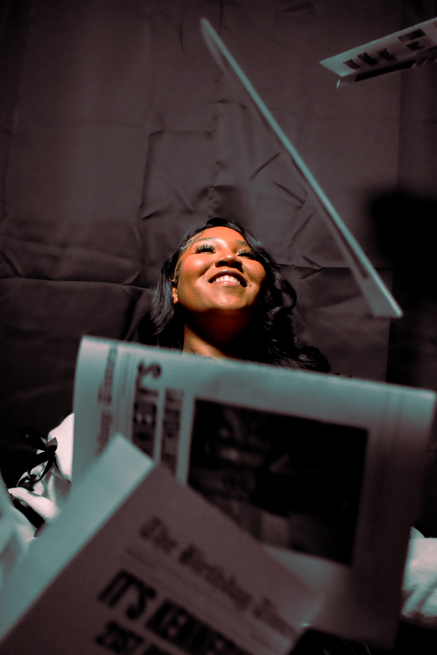 Woman smiling as birthday newspapers fall around her during a dramatic birthday photoshoot.