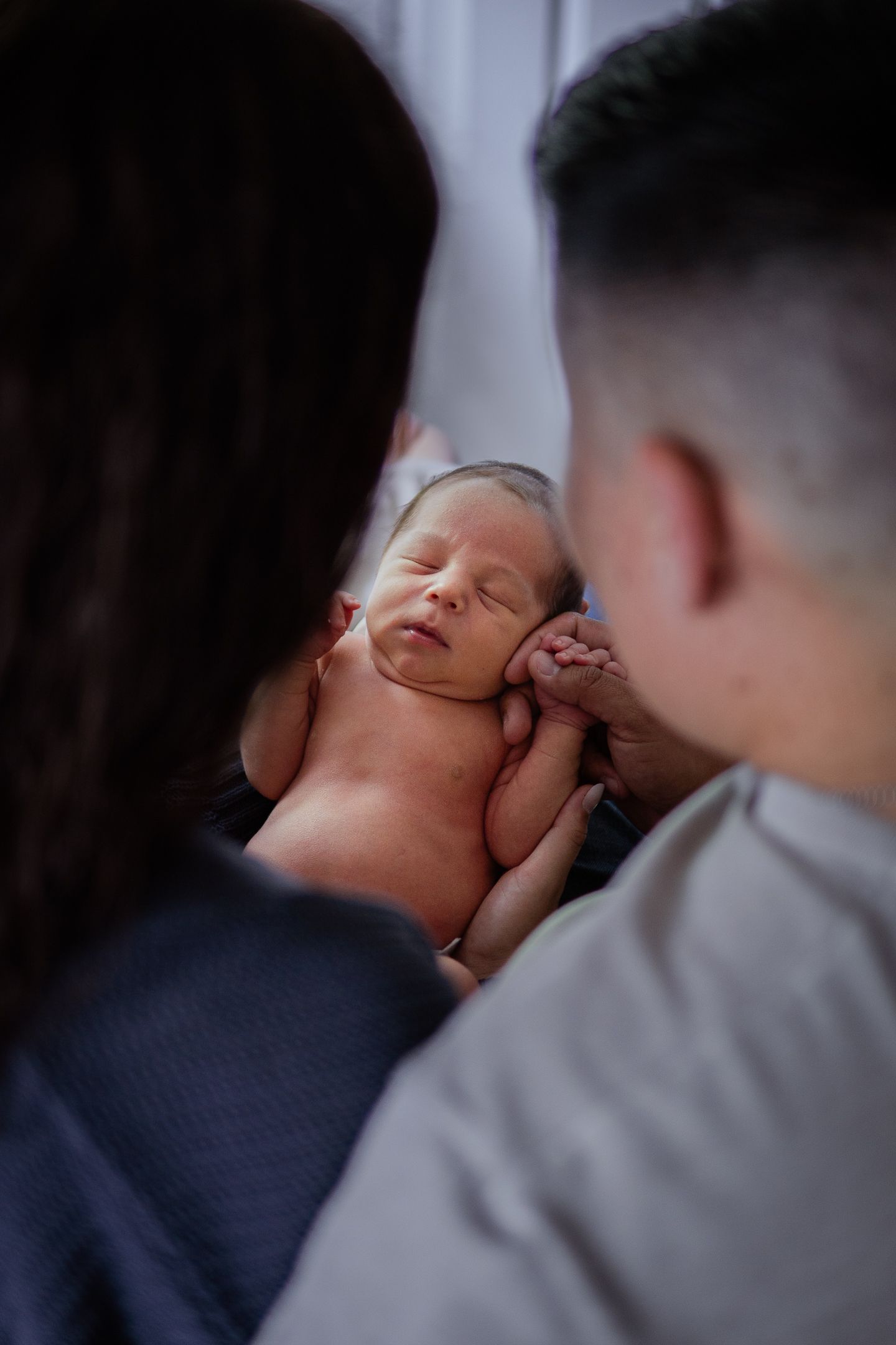 A sleeping newborn baby nestled between two parents in an intimate close-up portrait.